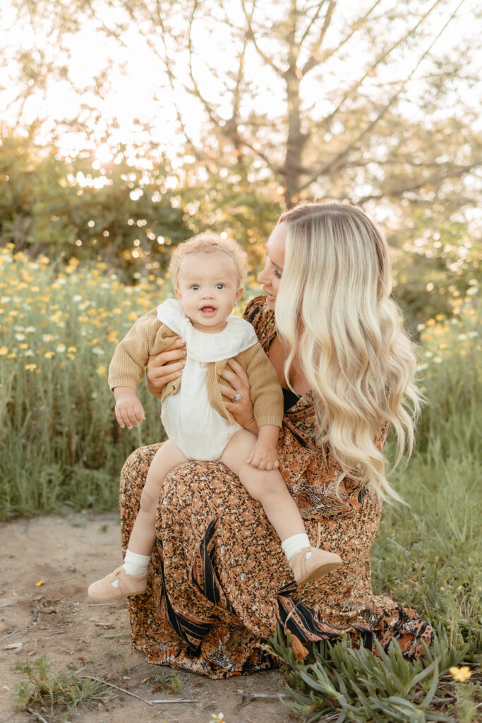 Milestone session in wildflowers with mother holding baby in soft golden light