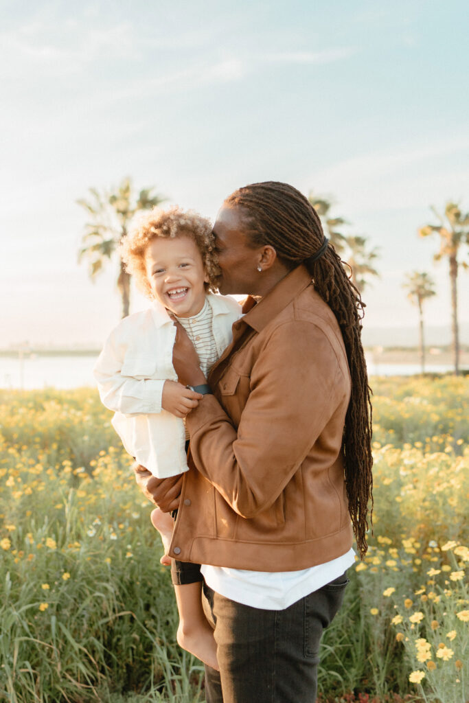 Family photographer capturing father holding child in wildflowers with natural light